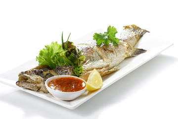 Roasted Whole Giant Sea Perch Fish (Pra-Kra-Pong) with Red Chili Garlic Seafood Sauce and a piece of lemon on white porcelain plate, isolated on white background with shadow, High angle side view