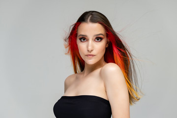 Naklejka premium A close-up portrait photo of a fashionable hairstyle red-yellow in studio on a blue background. The pretty brunette model with beautiful make-up has beautiful flowing colorful hair.