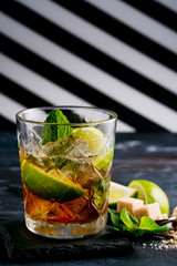 Whiskey and Cola cocktail with lime, mint, brown sugar and ice, alcoholic drink in a glass on a dark wooden background, copy space