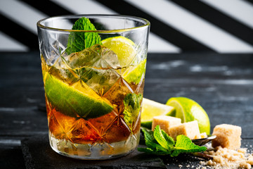 Whiskey and Cola cocktail with lime, mint, brown sugar and ice, alcoholic drink in a glass on a dark wooden background, copy space