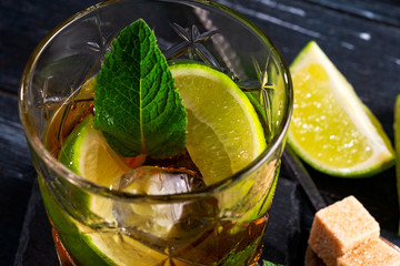 Whiskey and Cola cocktail with lime, mint, brown sugar and ice, alcoholic drink in a glass on a dark wooden background, copy space