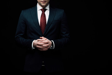 partial view of confident businessman standing with clenched hands isolated on black, human emotion...