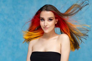 A close-up portrait photo of a fashionable hairstyle red-yellow in studio on a blue background. The...