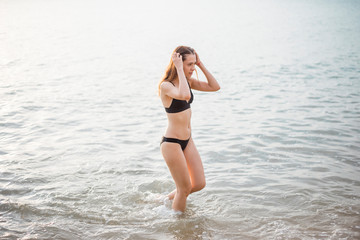 Beautiful woman in black bikini is enjoying with sea water on the beach