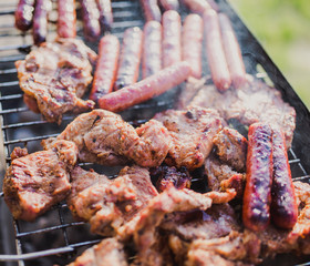Grilling sausages on barbecue grill. Pork sausage and steak in smoke. Close-up view & Selective focus. 