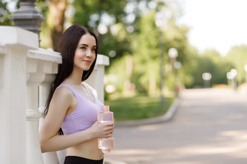 Beautiful slim brunette woman drinking water from bottle after running at the  morning park to stay hydrated. Female fitness model working out outdoor. Concept of healthy lifestyle.