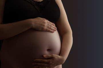 Pregnant woman holding a baby bump against a dark background