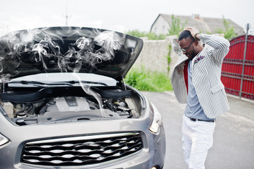 Stylish and rich african american man stand in front of a broken suv car needs assistance looking...