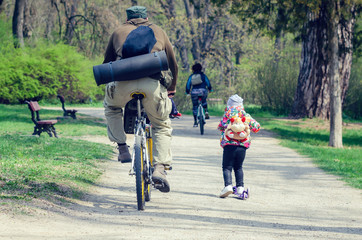 A man on a bicycle and a little girl on a scooter ride in the spring park.