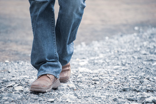 Feet walking of lonely man,step by step on the street.Picture of journey person wearing jean and fashion shoes (boot) along the path strew with rocks