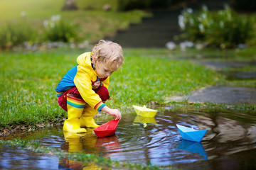 Child with paper boat in puddle. Kids by rain.