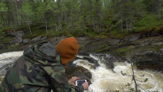Woman taking a photo of a cascade in a forest.
