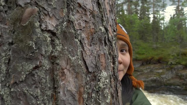 Woman playing and hiding behind a tree in a forest in slow motion.