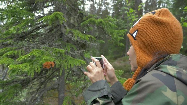 Slow motion shot of a woman taking pictures with a phone in a forest.