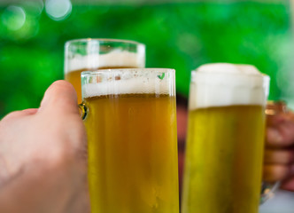 Close-up view of a three glass of beer in hand. Beer glasses clinking at outdoor bar or pub
