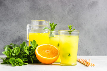 Orange lemonade in glass with fresh orange and mint over light grey stone table. Refreshing summer drink. Cocktail bar background concept. Copy space.