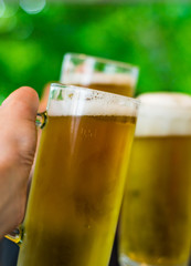 Close-up view of a three glass of beer in hand. Beer glasses clinking at outdoor bar or pub