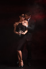 full length view of sensual bdsm couple with glass on champagne embracing on black