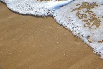 ocean wave washing up onto a brown sandy beach forming foam