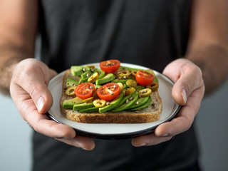 Hands takes plate with vegan sandwich. Healthy appetiezer - whole wheat bread toast with avocado,...