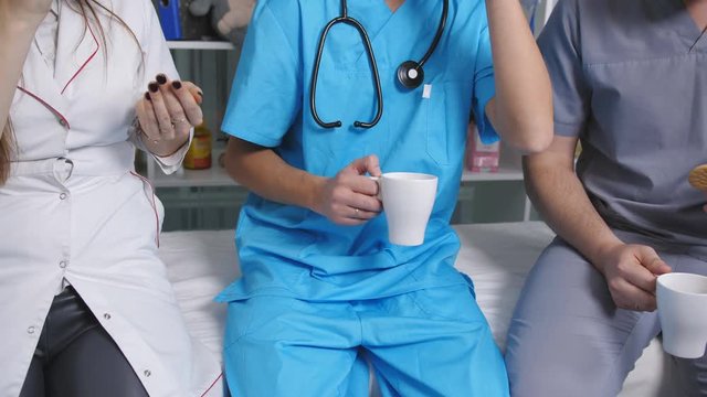 Three doctors in the staffroom talk and drink coffee at the break.