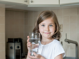 Healthy lifestyle. Portrait of happy smiling young girl with glass. Child drinking fresh water in the kitchen at home, looking at camera. Healthcare. Drinks. Health, beauty, diet concept. Good eating