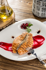 close up of grilled salmon steak with cranberries and red sauce on wooden table