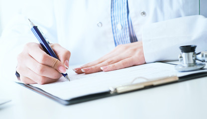 Female medicine doctor hand holding silver pen writing something on clipboard close-up.. Ward round, patient visit check, medical calculation and statistics concept.