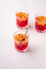 Jelly dessert with fruits apricot raspberry in three drinking glasses with single spoon yellow red summer white background isolated