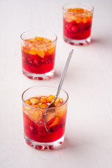 Jelly dessert with fruits apricot raspberry in three drinking glasses with single spoon yellow red summer white background isolated