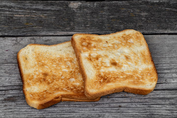 Two square ruddy pieces of bread for toasts on the old gray wooden background