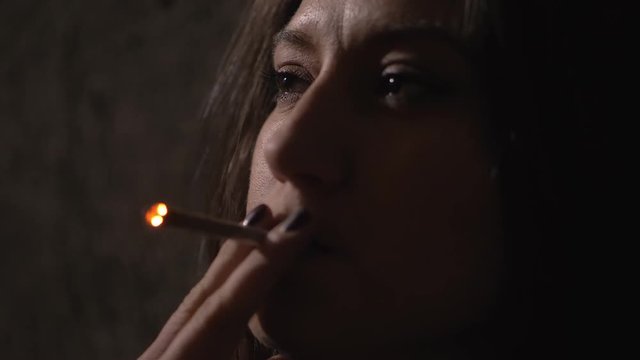 depressed pensive lonely young woman smoking joint in the dark.
