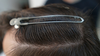 Closeup of hairdresser cutting man's hair in barber shop.Male hairstylist serving client, making haircut using hairpins and hair clips and comb.