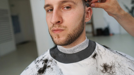Making hair look magical. Portret of young Bearded man sitting in chair at barbershop. Barber is trimming his hair with a straight razor. Closeup.