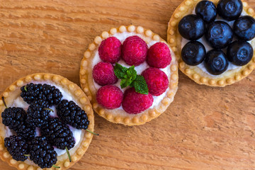 Basket-shaped cookies with raspberry, blueberry and blackberry berries. Wooden background