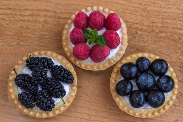 Basket-shaped cookies with raspberry, blueberry and blackberry berries. Wooden background