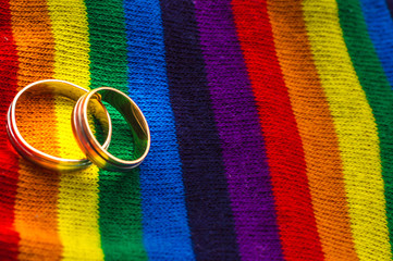 Two wedding rings on the fabric colors of the rainbow. Concept same-sex marriage. Cope space