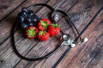 Red Scottish strawberries and black grapes with stethoscope on top of wooden table. Medical and...