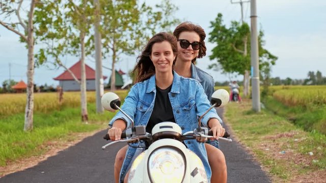 Joyful young women traveling by motorbike. Two cheerful laughing girlfreinds motorbike travelers portrait behind the sunset sea coast
