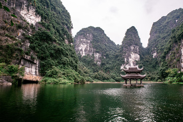 Fototapeta premium Boat cave tour in Trang An Scenic Landscape formed by karst towers and plants along the river (UNESCO World Heritage Site). It's Halong Bay on land of Vietnam. Ninh Binh province, Vietnam.