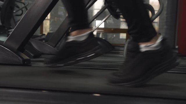 Close up feet of man walking at brisk pace on treadmill at the gym, tracking left.