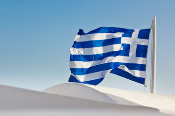 Closeup of a waving flag of Greece over the white round roofs of Santorini, Greece