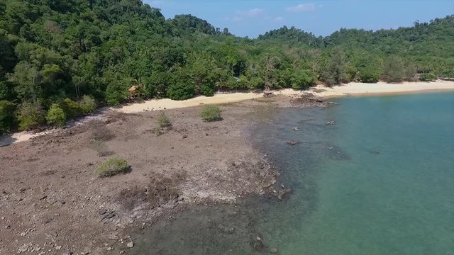 An high angle shot of a rocky and sandy beach sandwiched in between a dense forest and a sea on the other side in a place in Thailand .
