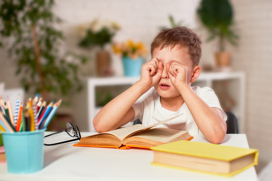 The Child Is Tired Of Learning. Home Schooling, Homework. The Boy Rubs His Eyes From Fatigue Reading Books And Textbooks. Vision Problems