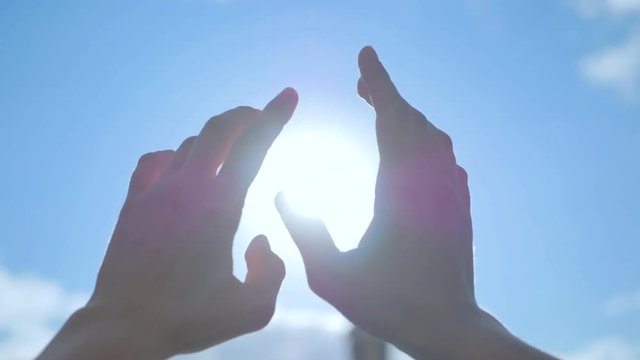 SLOW MOTION, CLOSE UP: Unrecognizable woman catching setting sun with her heart shaped fingers. Young girl making the symbol of love with her hands against stunning golden sky and rising morning sun.