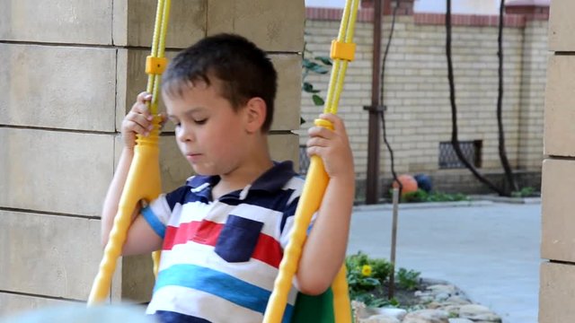 A young boy swing set in a park. The small child is having fun, smiling. It is summer time at the playground. He is wearing a t-shirt and shorts and is laughing.