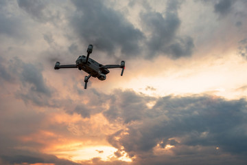 Drone quadcopter with digital camera flying at sunset.