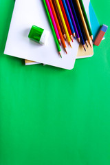 Multicolored pencils, notebooks, eraser and sharpener on a green background with space for text. School set. Flat lay
