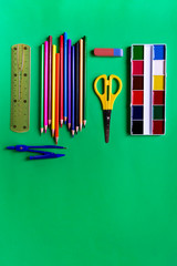 Collection of school supplies from paints, pencils, scissors, ruler, eraser and compasses on a green background with copy space.Flat lay
