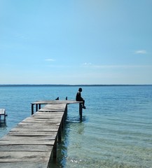 Naklejka premium Mężczyzna siedzący na molo oglądając zachód słońca